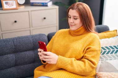 Young beautiful plus size woman using smartphone sitting on sofa at home