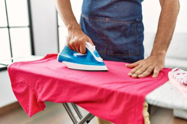 Orta yaşlı, kır saçlı, evde giysilerini ütüleyen bir adam.