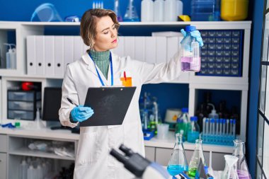 Young woman scientist reading report holding test tube at laboratory