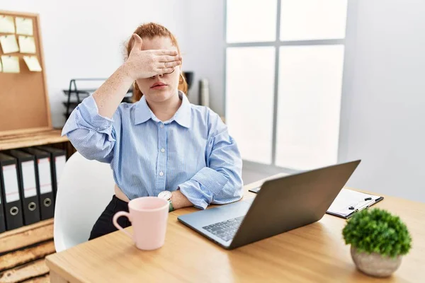 在办公室里工作的红头发年轻女人用手提电脑蒙住眼睛 看起来严肃而忧郁 躲藏和拒绝的概念 — 图库照片