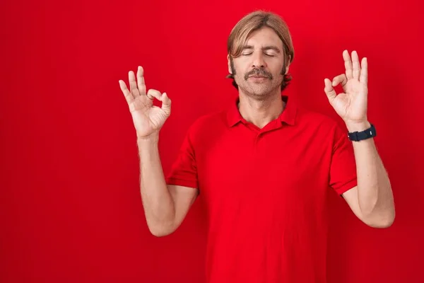 白种人留着胡子 站在红色的背景上放松 闭上双眼微笑 用手指做冥想动作 瑜伽概念 — 图库照片