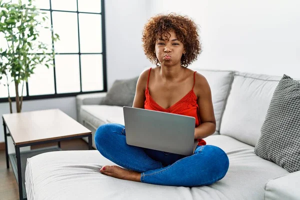 Młoda Afroamerykanka Siedząca Kanapie Domu Używająca Laptopa Nadymającego Policzki Śmieszną — Zdjęcie stockowe