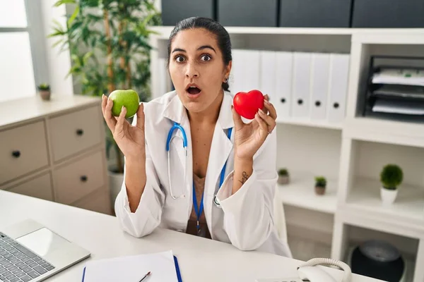 Young Hispanic Woman Working Dietitian Clinic Holding Green Apple Afraid —  Fotos de Stock