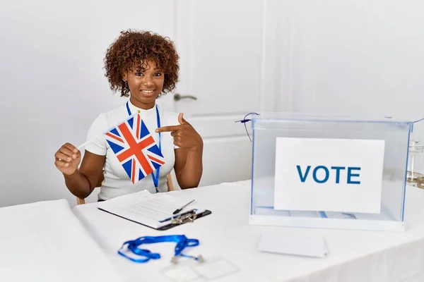Young african american woman at political campaign election holding uk flag smiling happy pointing with hand and finger