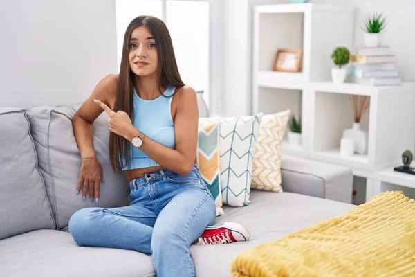 年轻的黑发女人坐在家里的沙发上 用食指 关心和惊讶的表情 把焦虑和紧张放在一边 — 图库照片
