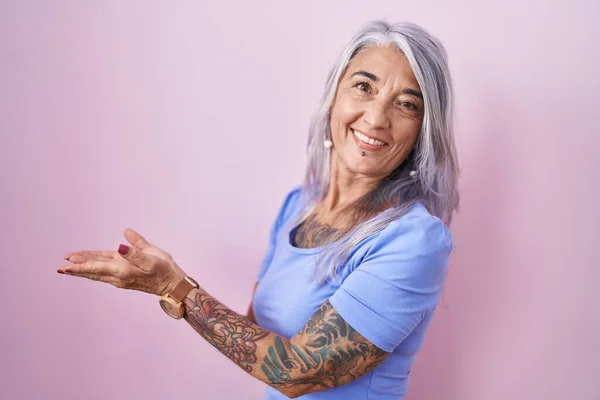 Medelålders Kvinna Med Tatueringar Står Över Rosa Bakgrund Pekar Sidan — Stockfoto
