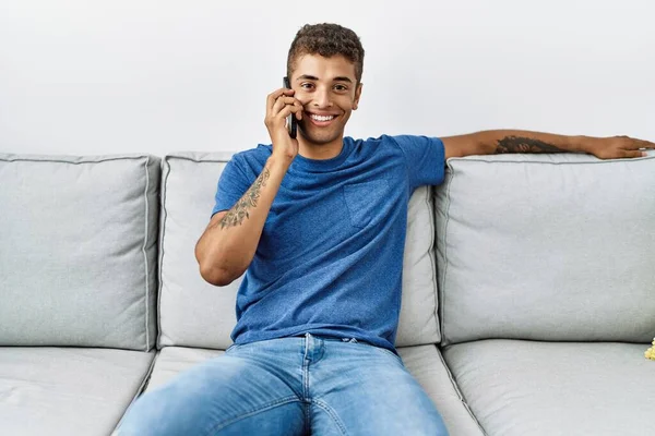 Joven Hombre Hispano Relajado Sentado Sofá Hablando Por Teléfono Casa —  Fotos de Stock