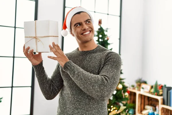 Young Hispanic Man Holding Gift Standing Christmas Tree Home — Stok fotoğraf