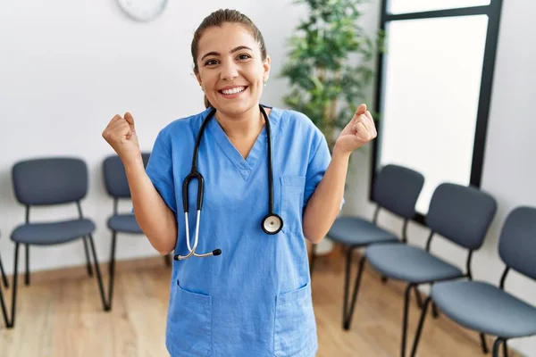 Young brunette doctor woman at waiting room screaming proud, celebrating victory and success very excited with raised arms