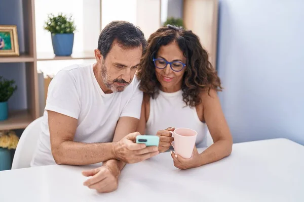 Man and woman couple drinking coffee using smartphone at home