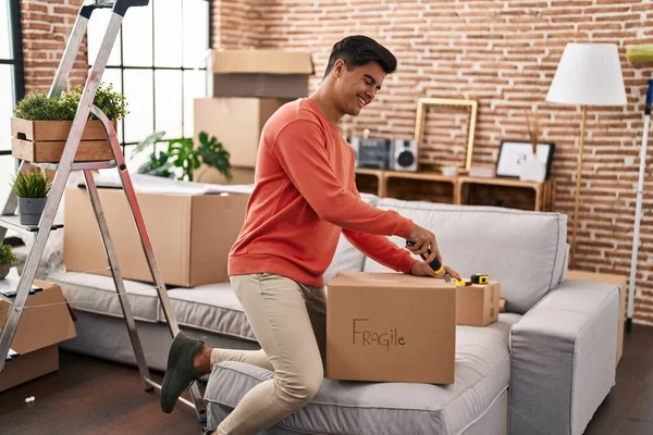 Young Hispanic Man Smiling Confident Unpacking Cardboard Box New Home — ストック写真