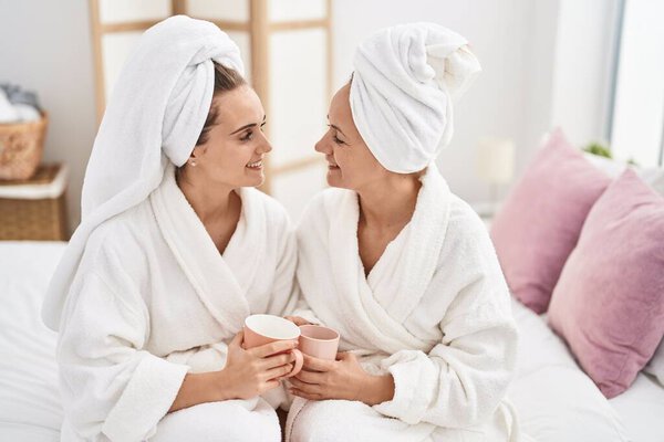 Two women mother and daughter wearing bathrobe drinking coffee at bedroom