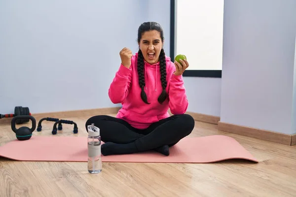 Young Hispanic Woman Sitting Yoga Mat Eating Apple Annoyed Frustrated — Stockfoto