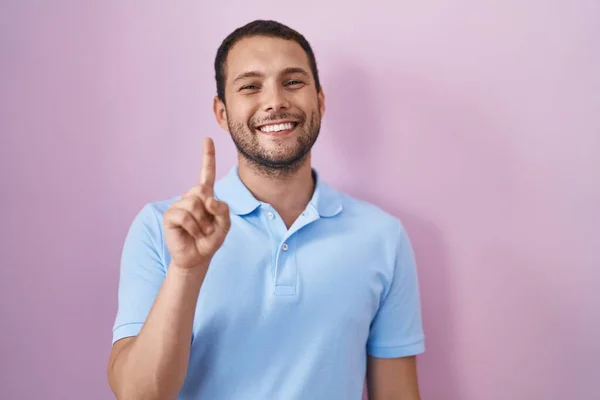 ヒスパニック男立ち上がっピンクの背景表示と指差し込みとともに指第一位ながら笑顔自信と幸せ — ストック写真