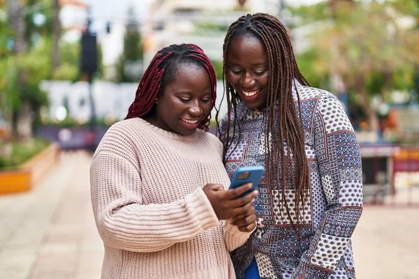 アフリカ系アメリカ人の女性が自信を持って笑顔で公園でスマートフォンを使う — ストック写真