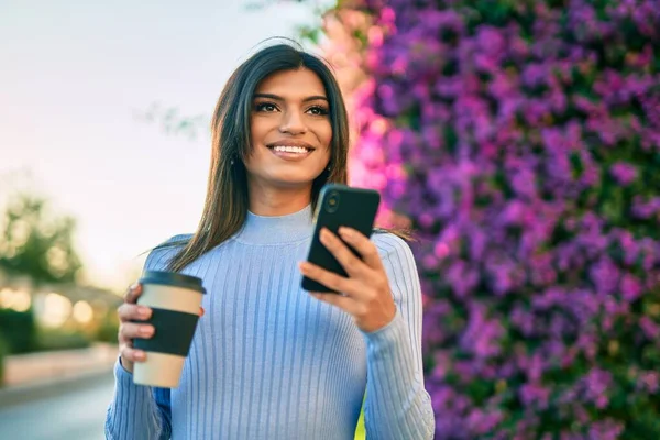 公園のそばでコーヒーを飲みながらスマホを使っている若いヒスパニック系の女性 — ストック写真