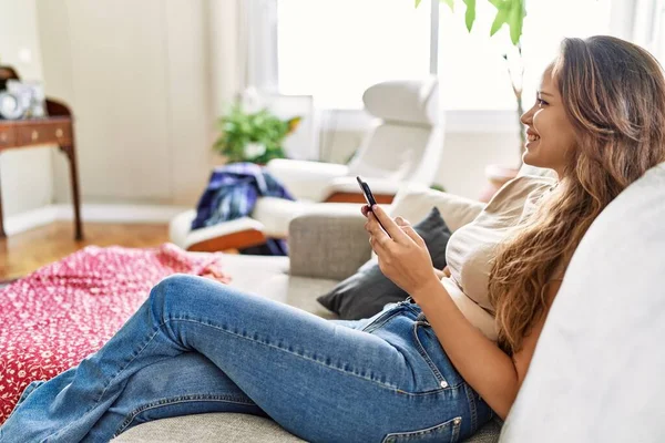 年轻的惊慌失措的姑娘坐在家里的沙发上用智能手机 — 图库照片