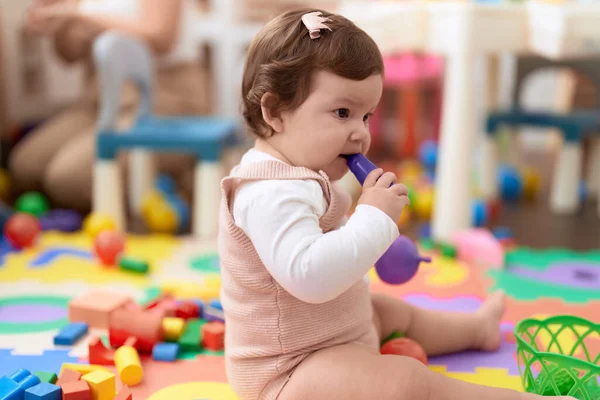 Adorable toddler bitting plastic food toy sitting on floor at kindergarten