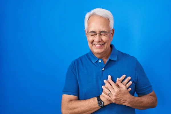 一个白发苍苍的中年男人站在蓝色的背景上微笑着 双手放在胸前 闭着眼睛 脸上挂着感激的手势 健康概念 — 图库照片