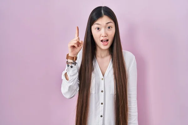 中国年轻女子站在粉红的背景上 指指点点 想出了个好主意 又兴奋又快乐第一大 — 图库照片