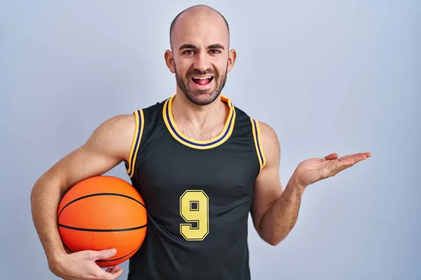 Mladý Plešatý Muž Plnovousem Basketbalové Uniformě Drží Míč Ukazuje Stranou — Stock fotografie