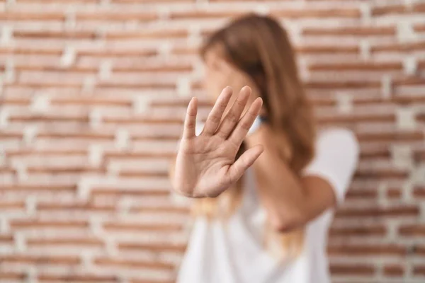 Young caucasian woman standing over bricks wall covering eyes with hands and doing stop gesture with sad and fear expression. embarrassed and negative concept.
