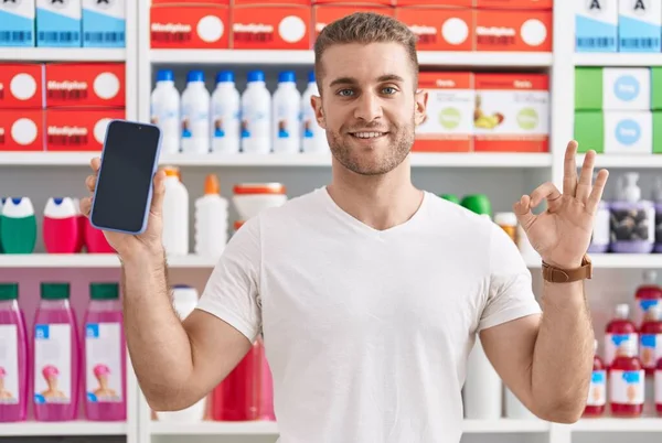 Young Caucasian Man Working Pharmacy Drugstore Showing Smartphone Screen Doing — Stockfoto