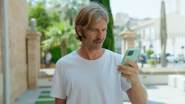 年轻的金发男子在街上用带有严肃表情的智能手机 — 图库照片