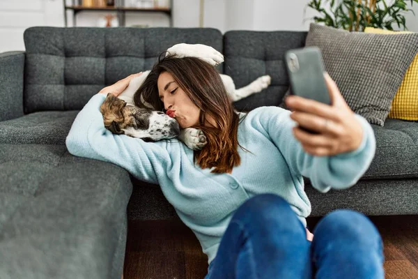 在家里 年轻的女人靠智能手机亲吻和拥抱自己的狗 — 图库照片