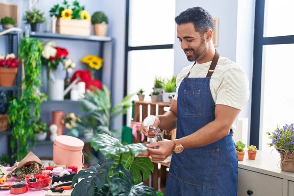 Young hispanic man florist smiling confident watering plant at florist