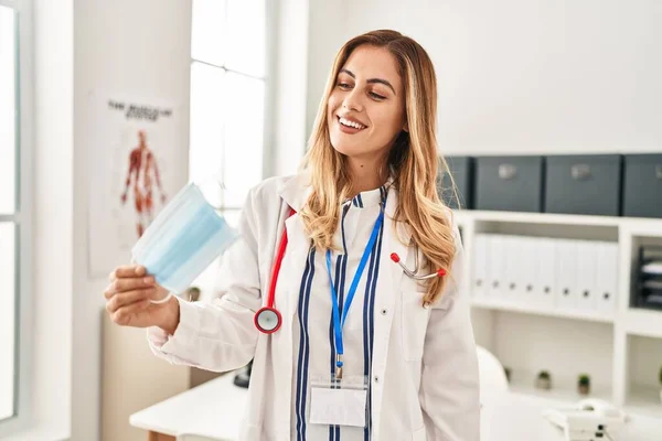 Young Blonde Woman Wearing Doctor Uniform Holding Medical Mask Clinic — Stock Photo, Image