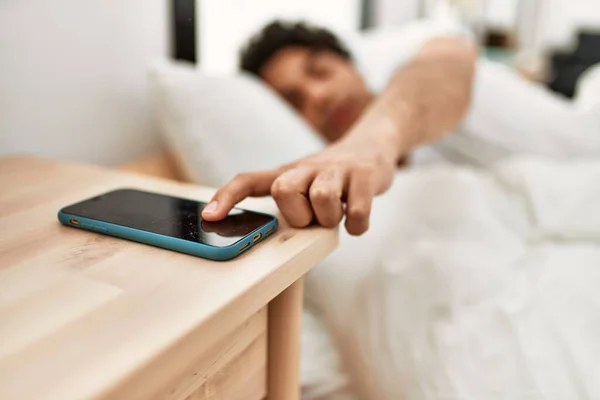 年轻的惊慌失措的男人关掉躺在卧室床上的智能手机警报 — 图库照片