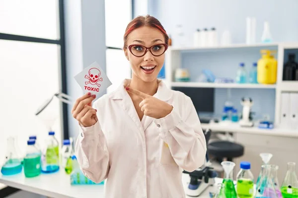 Joven Mujer Caucásica Trabajando Laboratorio Científico Sosteniendo Etiqueta Tóxica Sonriendo —  Fotos de Stock