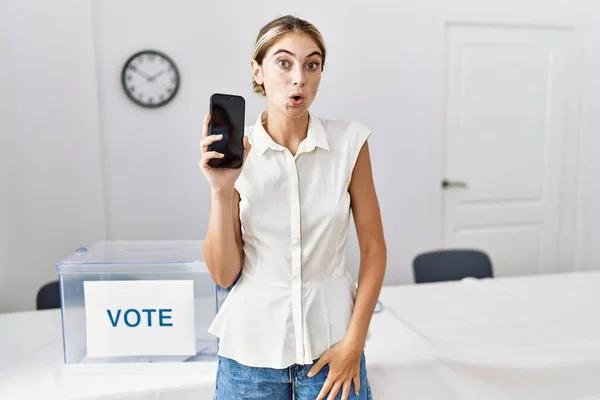 Młoda Blondynka Wyborach Politycznych Trzyma Smartfona Przerażony Zdumiony Otwartymi Ustami — Zdjęcie stockowe