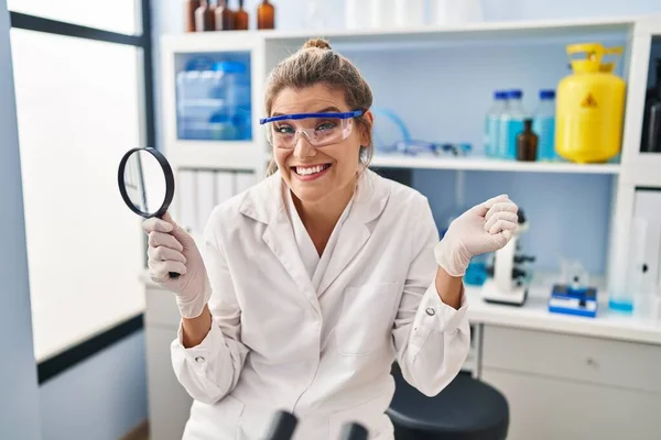 科学者研究所で働く若い女性は誇りを持って叫んで虫眼鏡を保持します 勝利と成功を祝う非常に腕を上げ興奮して — ストック写真