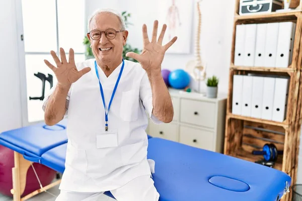 自信満々で笑顔ながら指の数10を見せ指摘しながら痛み回復クリニックで働く先輩理学療法士 — ストック写真