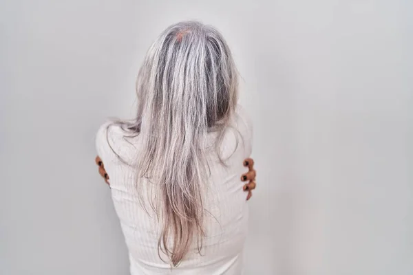 白发苍苍的中年妇女站在白种人的背景上 高兴地拥抱着自己 从后面又是积极的 自爱和自我照顾 — 图库照片