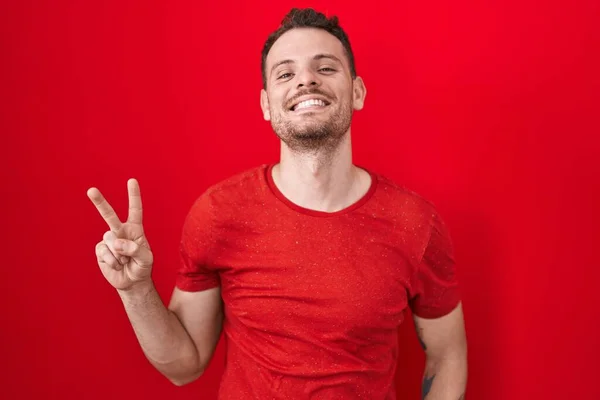 Mladý Hispánec Stojící Nad Červeným Pozadím Usmívající Kameru Ukazující Prsty — Stock fotografie