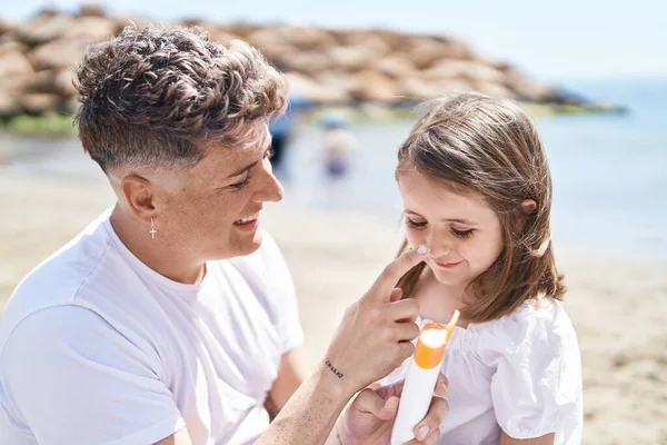 Father and daughter applying sunscreen sitting on sand at beach