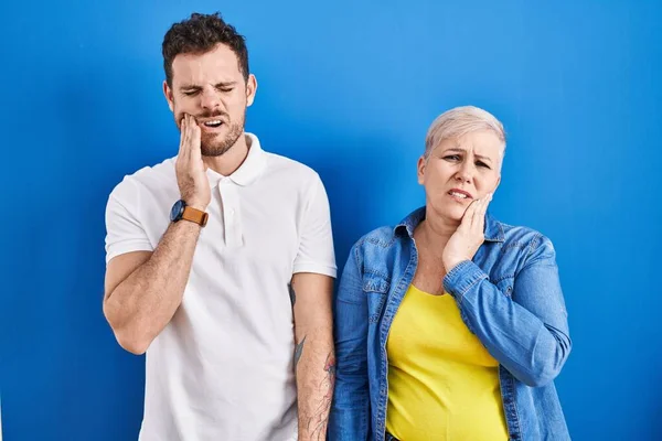 歯痛や歯の病気のため 若いブラジル人の母親と息子は痛みを伴う表現で手で口に触れる青の背景に立っている 歯科医 — ストック写真