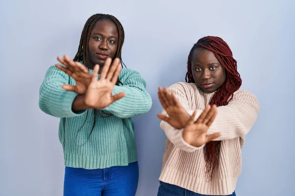 Две Африканки Стоят Синем Фоне Отвергая Выражение Лица Скрещивая Руки — стоковое фото