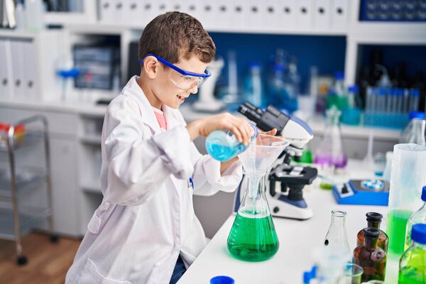 Blond child wearing scientist uniform measuring liquid at laboratory