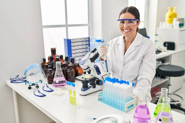 stock image Young beautiful hispanic woman scientist smiling confident pouring liquid on test tube at laboratory