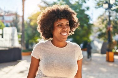 Afro-Amerikalı kadın gülümsüyor, parkın kenarına bakıyor.