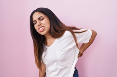 Young arab woman standing over pink background suffering of backache, touching back with hand, muscular pain 