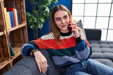 Evdeki koltukta oturan akıllı telefondan konuşan genç bir kadın.