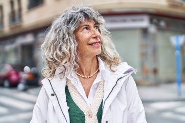 Orta yaşlı bir kadın sokakta kendine güvenerek gülümsüyor.