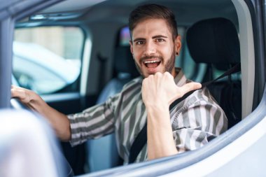 Sakallı, araba süren, ağzı açık gülümseyen İspanyol bir adam. 