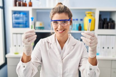 Laboratuvarda test tüpleri tutan bilim adamı üniforması giyen genç sarışın kadın.