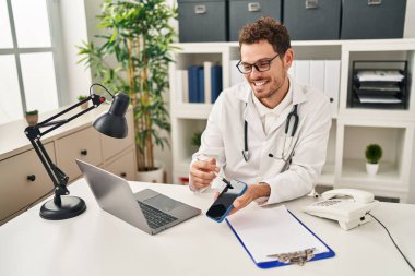 Doktor üniforması giyen genç İspanyol adam klinikte akıllı telefon olduğunu gösteren teletıp taşıyor.